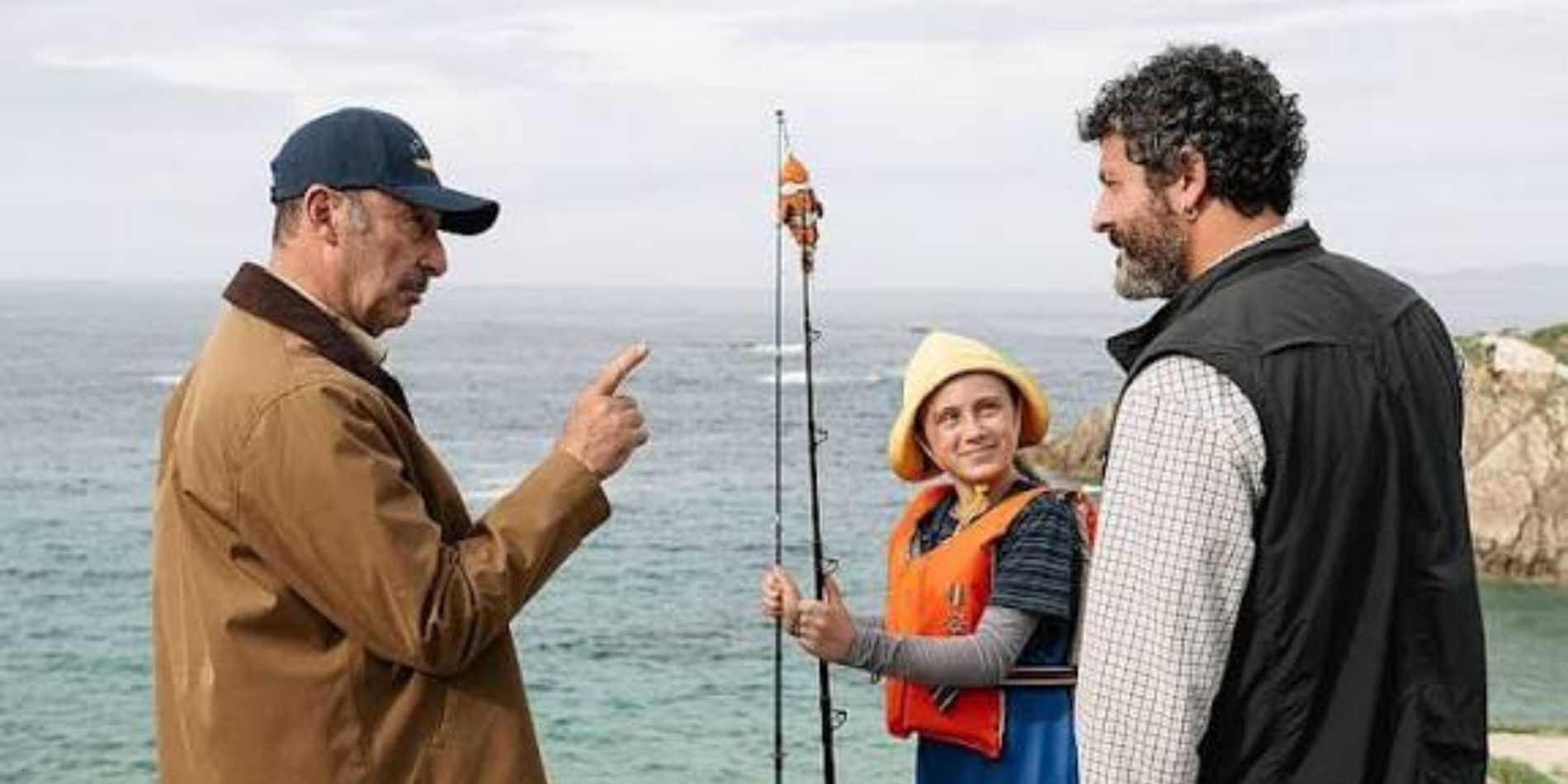 שלוש דמויות עומדות על רקע הים ומשוחחות ליד חוף סלעי, בעוד ילדה לבושה באפוד הצלה מחזיקה חכת דיג ומתבוננת באחד הגברים בחיוך. האווירה נינוחה ואנושית, ומשלבת תחושת מסע, מפגש בין דורות וקשר הנרקם בין הדמויות.